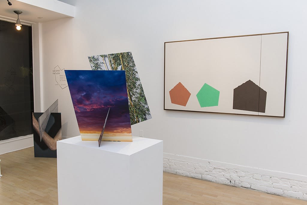 Exhibition installation view featuring abstracted sculptural work in foreground, paintings in background