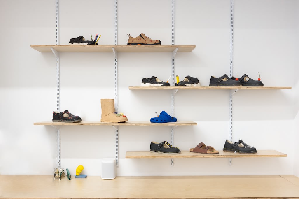 Installation of Didi Rojas exhibition - various shoe sculptures on shelves against white wall