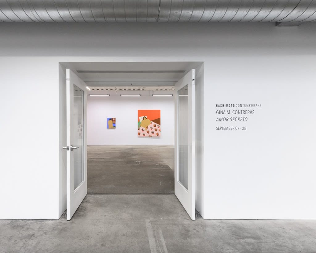 installation of Gina M. Contreras exhibition - two paintings visible from doorframe, wall vinyl on white walls to left reading 'Hashimoto Contemporary, Gina M. Contreras Amor Secreto, September 7 - 28'