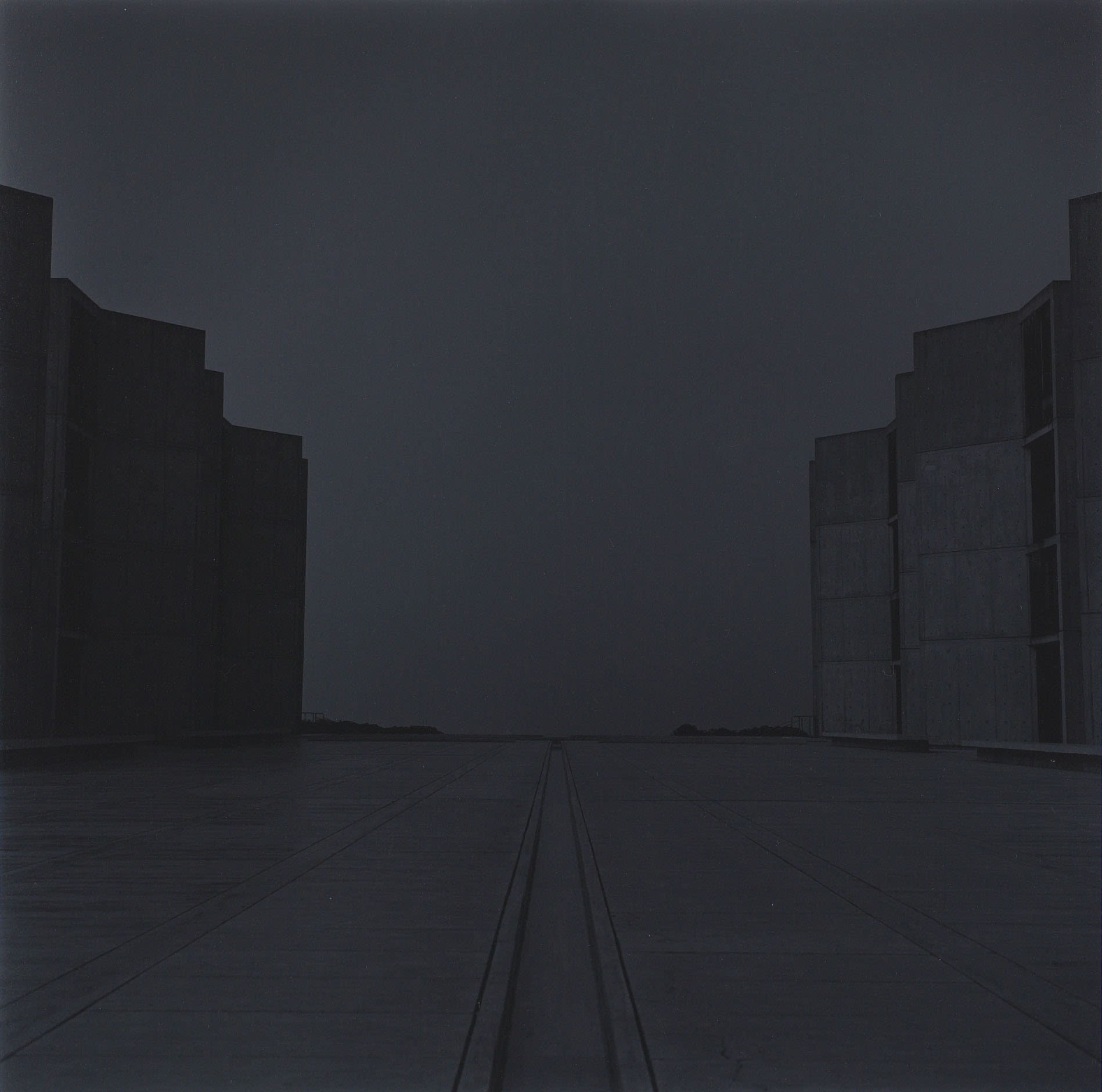 photograph of road between two buildings, one dark and one light, at night with no lights