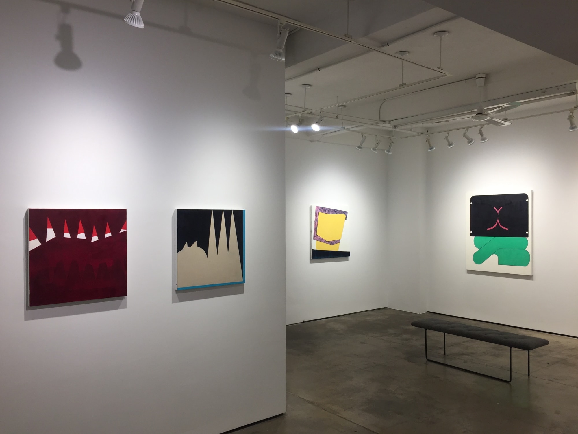 Gallery photograph of an installation featuring four different abstract paintings on canvases in shades of turquoise, tan, red, pink, blue, yellow and purple respectively.
