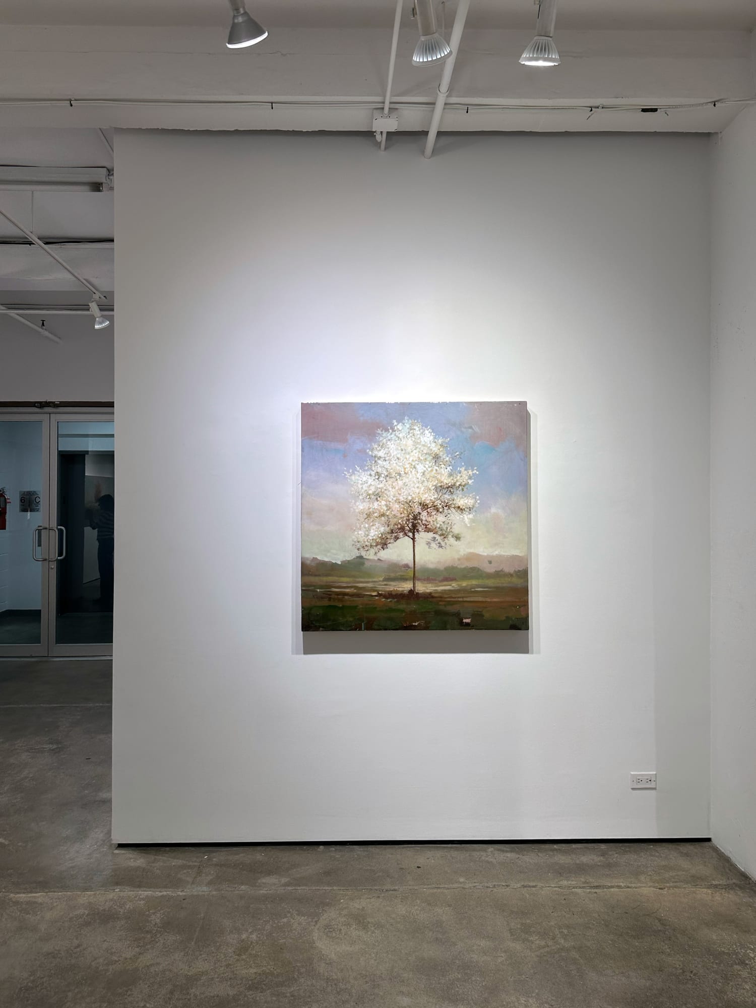 Photo of an installation with one painting visible. It is of a tree, framed symmetrically in the center of the canvas.