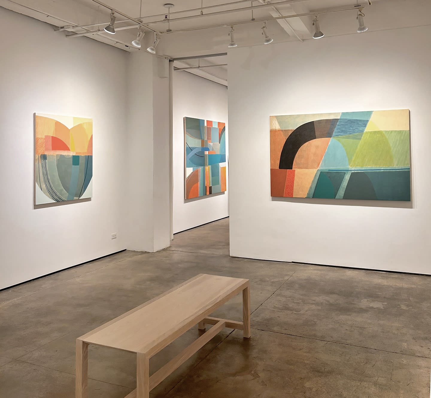 exhibition with three large geometric abstract paintings, cool in tone, on the walls. There is a bench in the center of one of the rooms