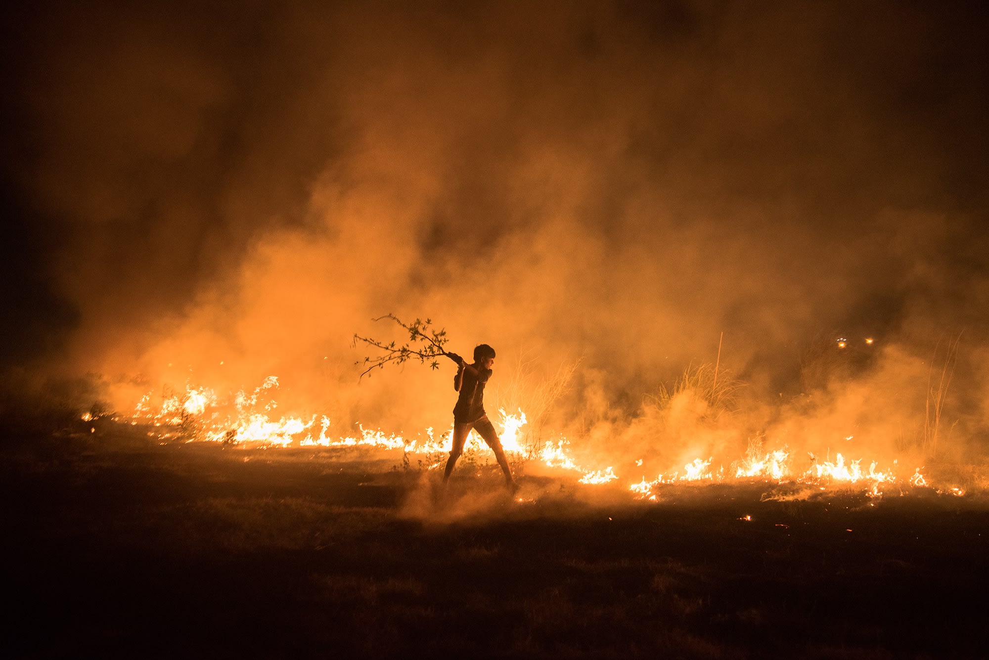 Landscape of fire, a young boy can be seen fighting like a mad beast against the fire that broke out near his home, picture by Amaan Ali