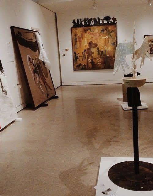 Paintings and sculptures are lined up against the wall, some with packing cloth over them.