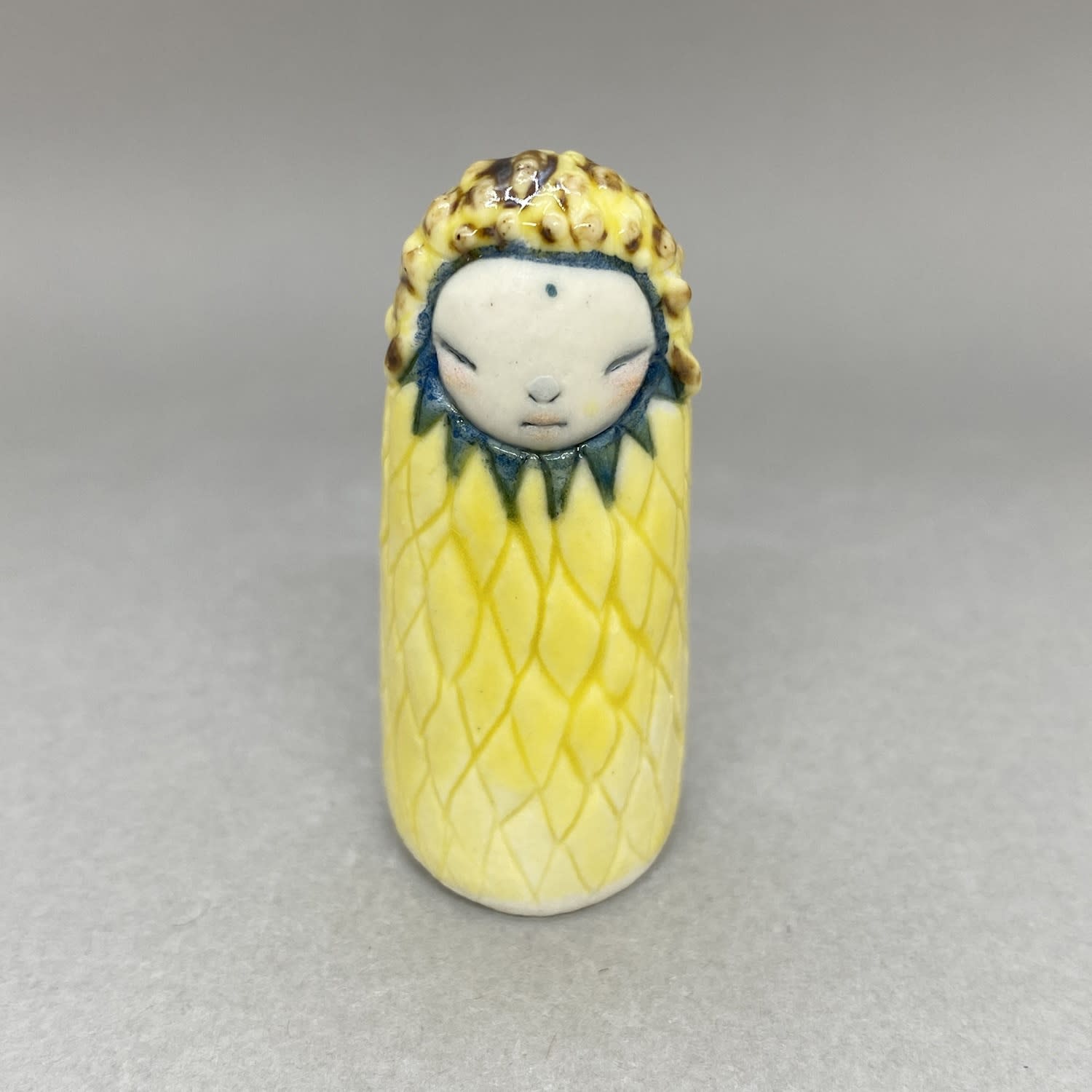 A tiny sculpture of a plant spirit in yellow with petal shape detail, blue petals around its face.