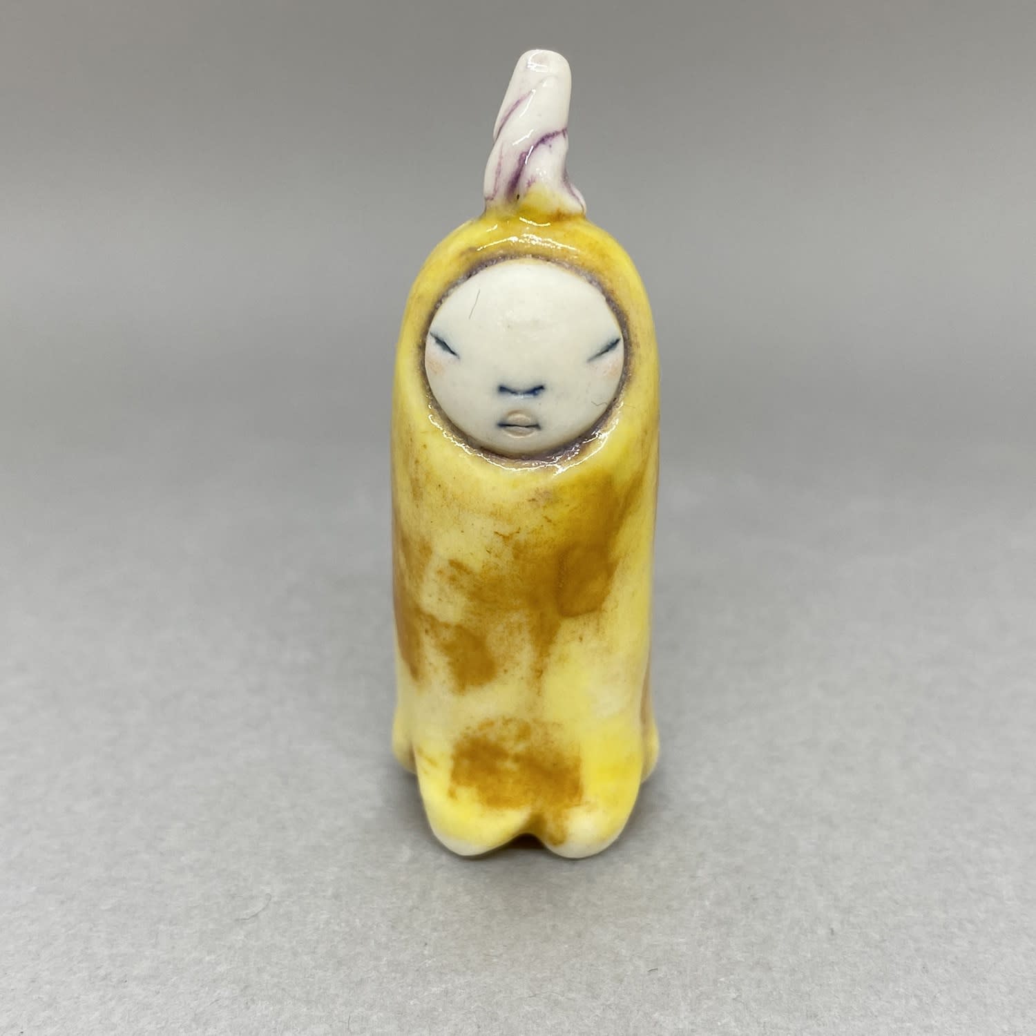 A tiny sculpture of a plant spirit in bright yellow and a purple seedling on its head.