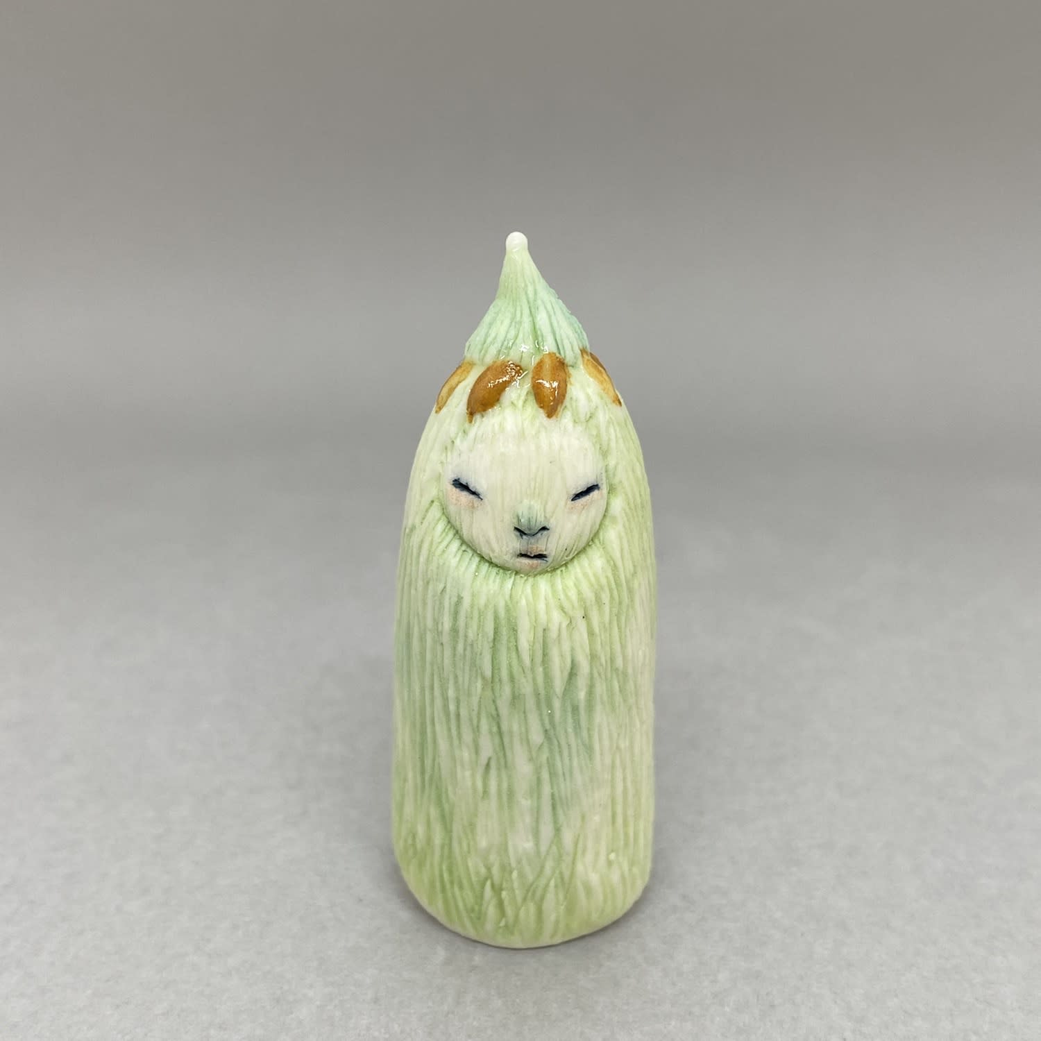 A tiny sculpture of a plant spirit in green with gold petal shapes on its head.