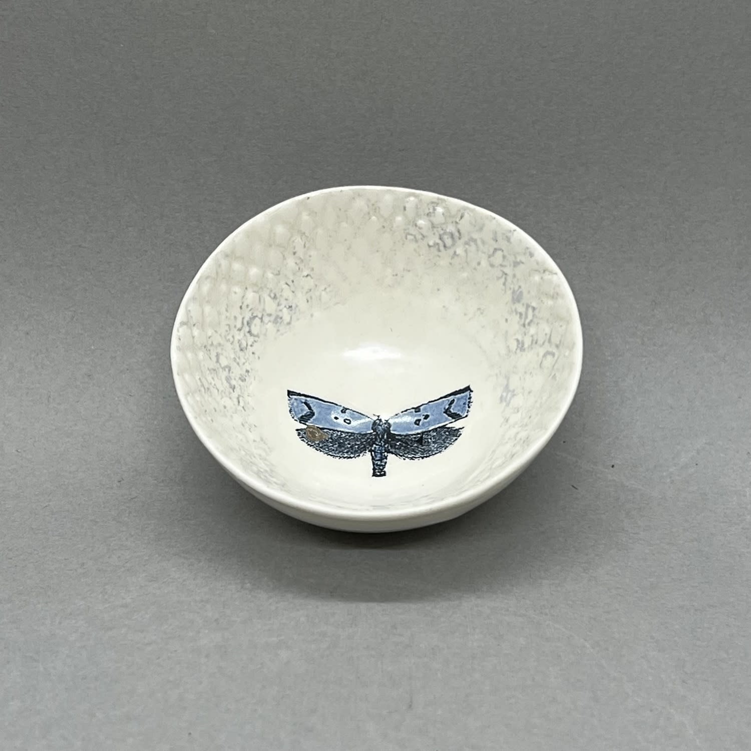 Fliff Carr ceramic bowl in white with blue lace detail printed round the edge and a small moth printed in the middle.