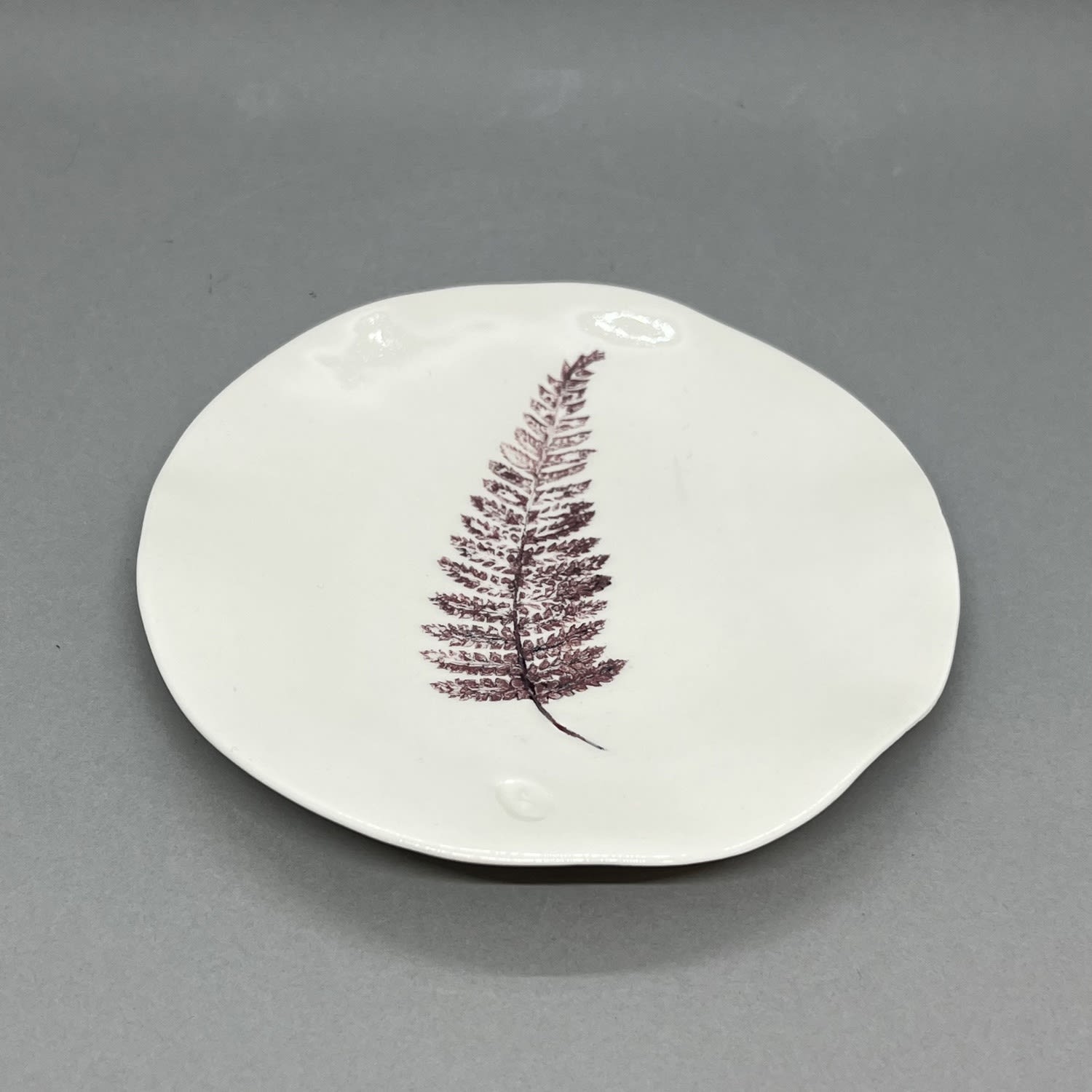 Fliff Carr white ceramic plate with maroon coloured fern leaf design printed on.