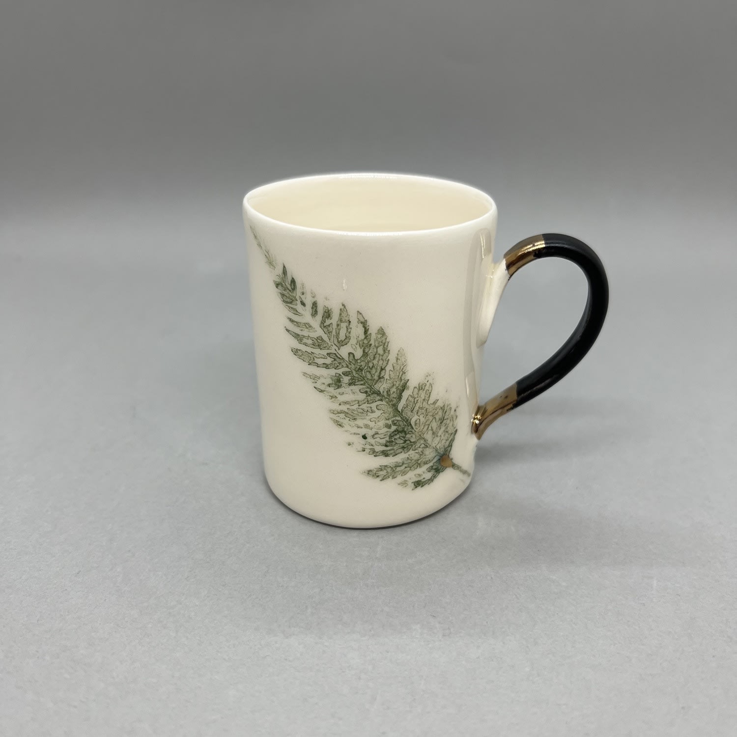 Fliff Carr white ceramic with printed fern leaf design each side and black and gold handle.