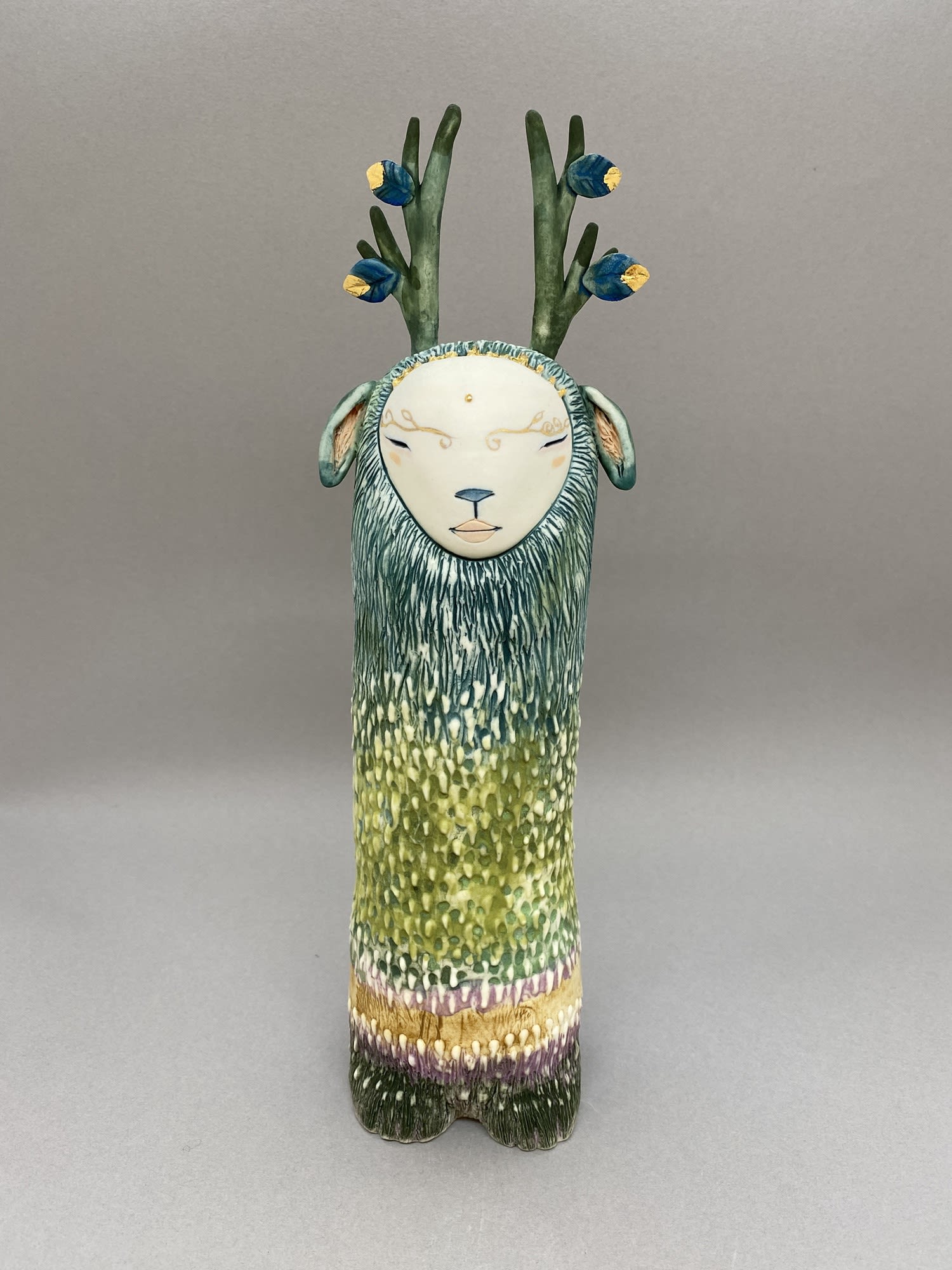 Inspired by Japanese kami culture, a figure in teal blue and green with gold antlers.