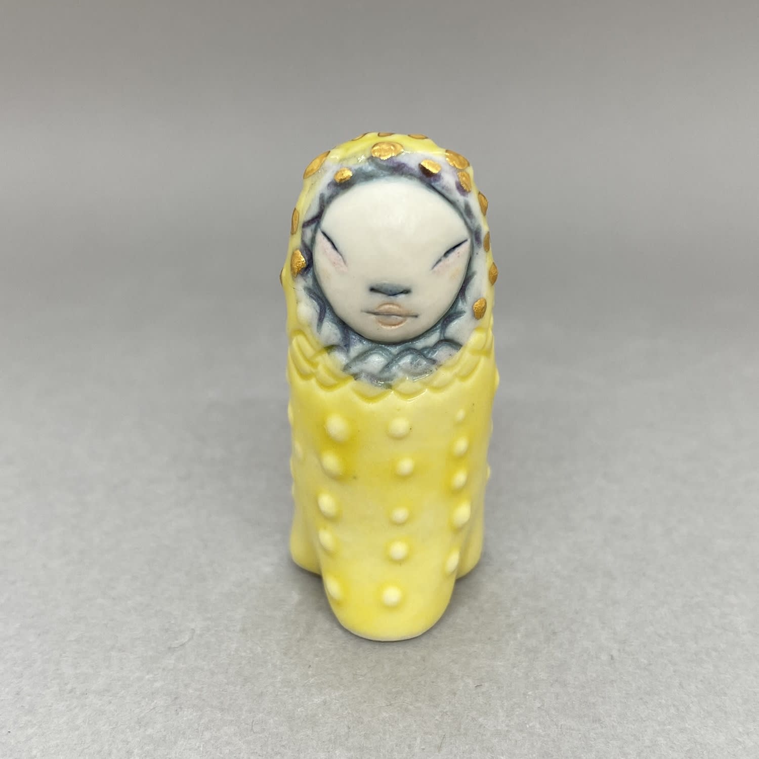 A tiny sculpture of a plant spirit in bright yellow with highlights in blue around its face.