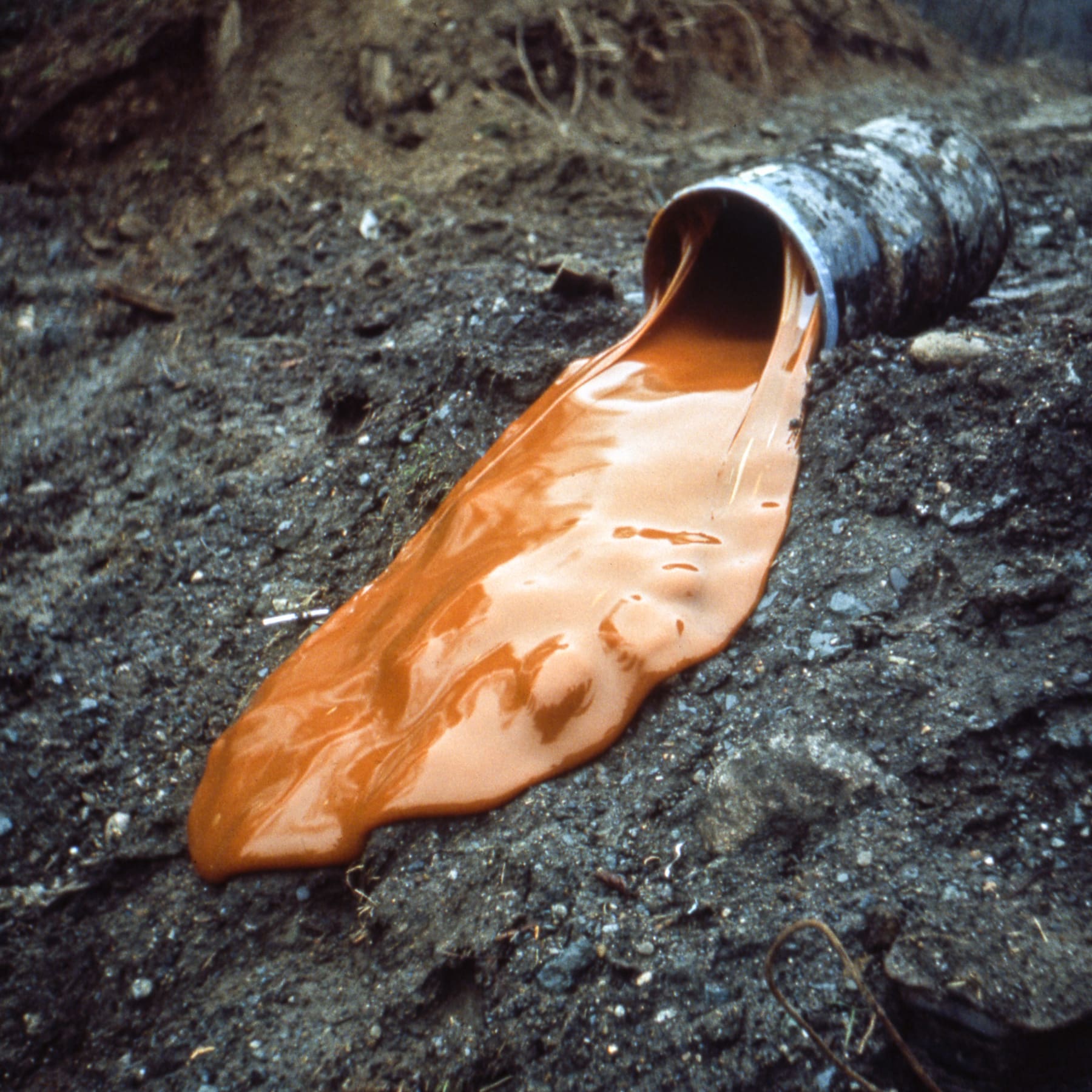 An image containing a large drum of glue at the crest of a hill and a tipped container. Earthwork by Robert Smithson