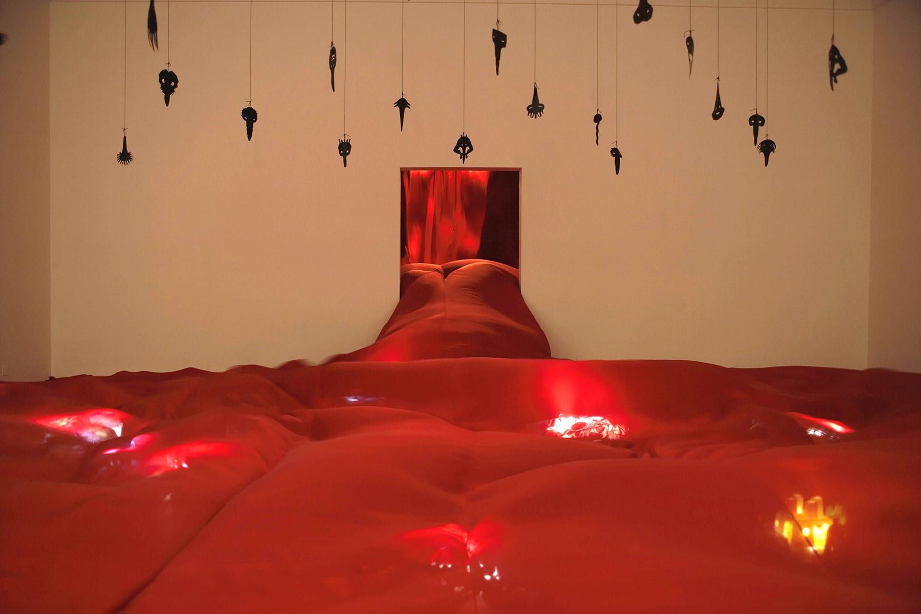 small black sculptures by Annette Messager hanging in a room with a red velvet bed