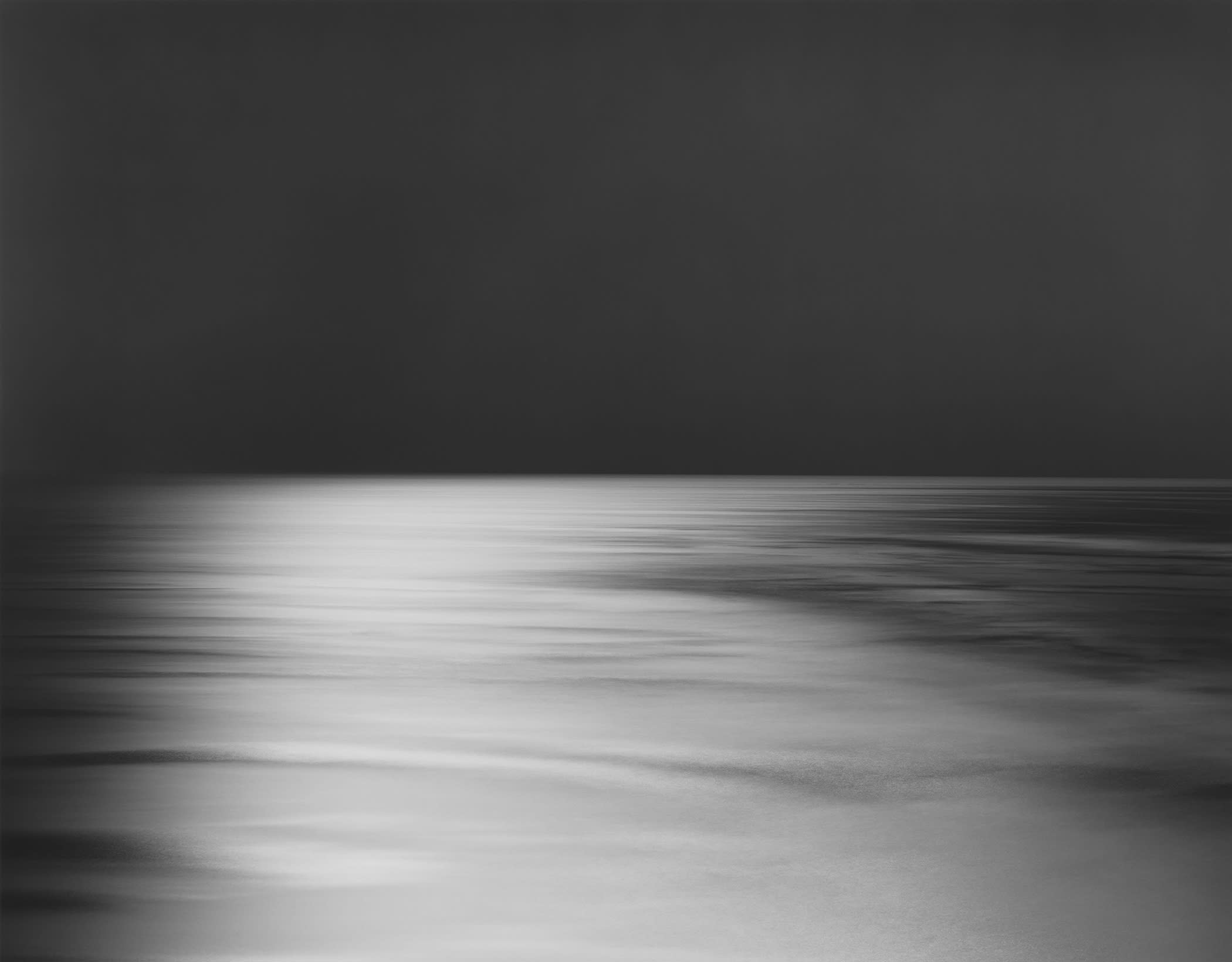 A Hiroshi Sugimoto photograph: A grayscale image of a horizon line with a dark sky and lighter ground.
