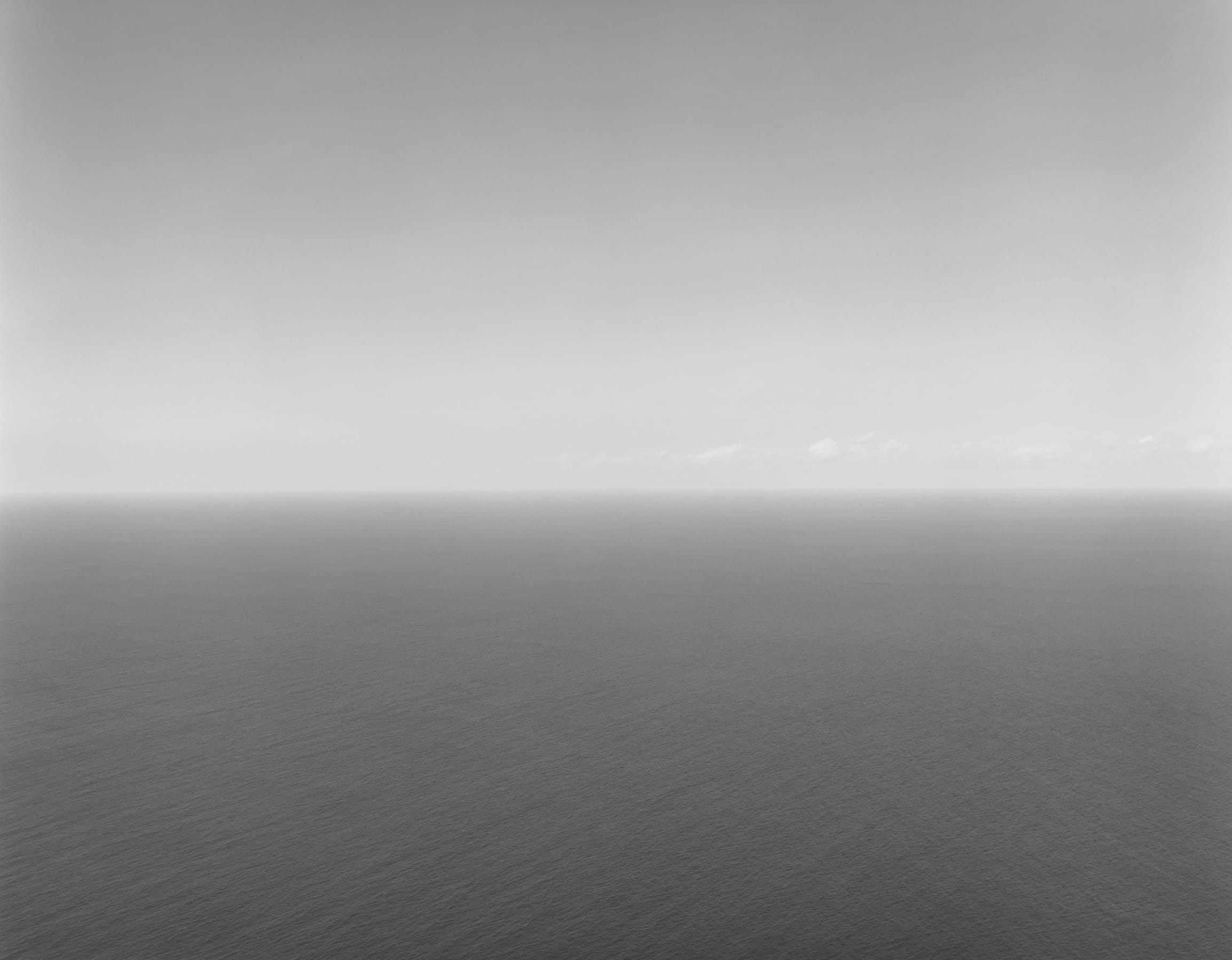 A Hiroshi Sugimoto photograph: A horizon line equally divides the frame between a light gray sky and darker body of calm water.