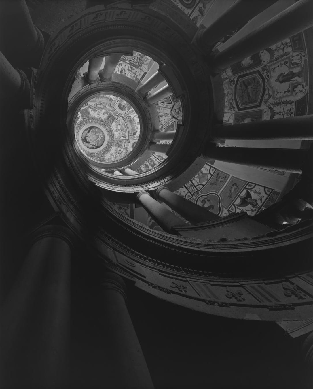 Black and white photograph of an upward view of a circular architectural spire with columns and fresco paintings in the grotesque style. 