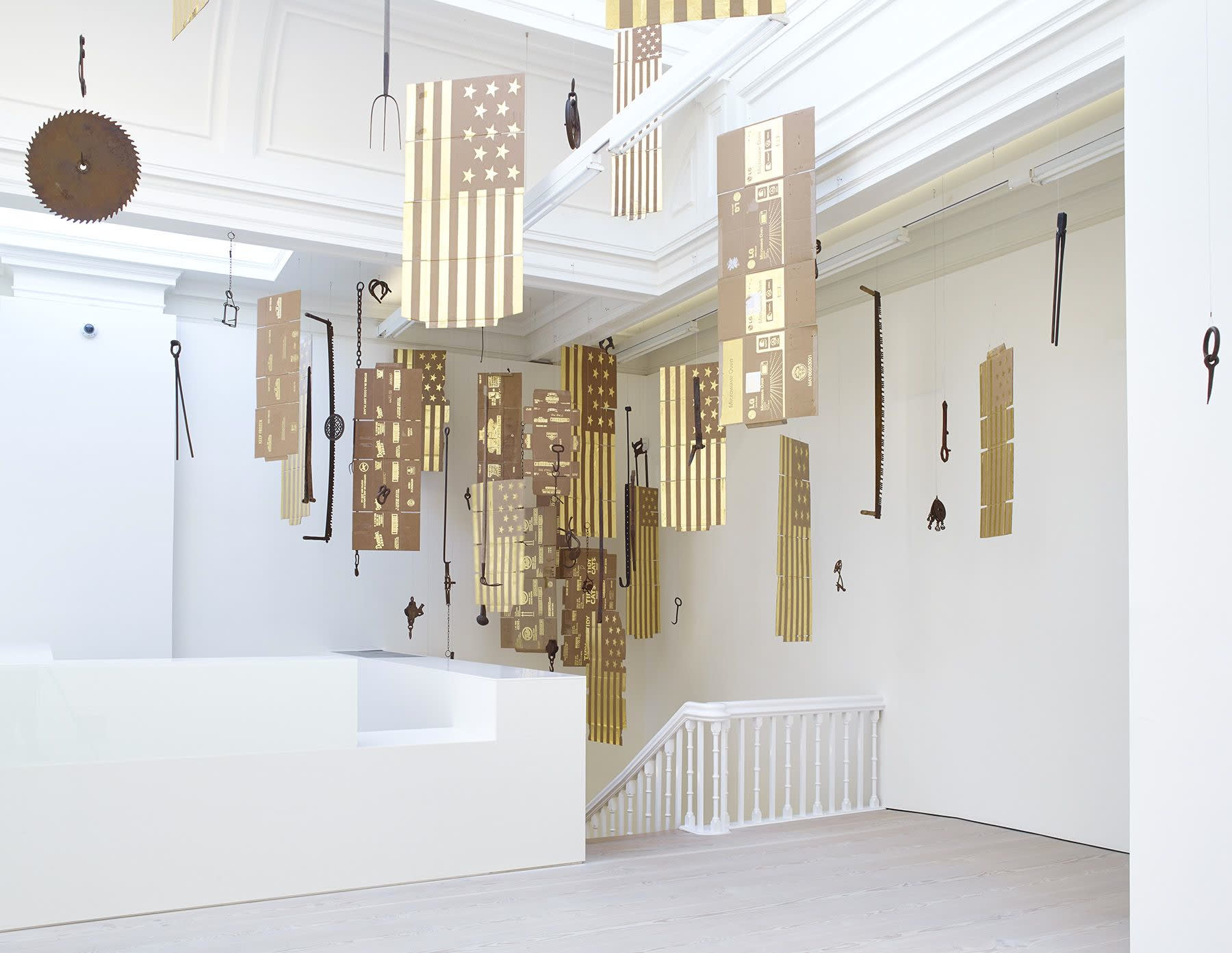 Gallery view of cardboard flags and numerous metal tools suspended from the gallery ceiling.