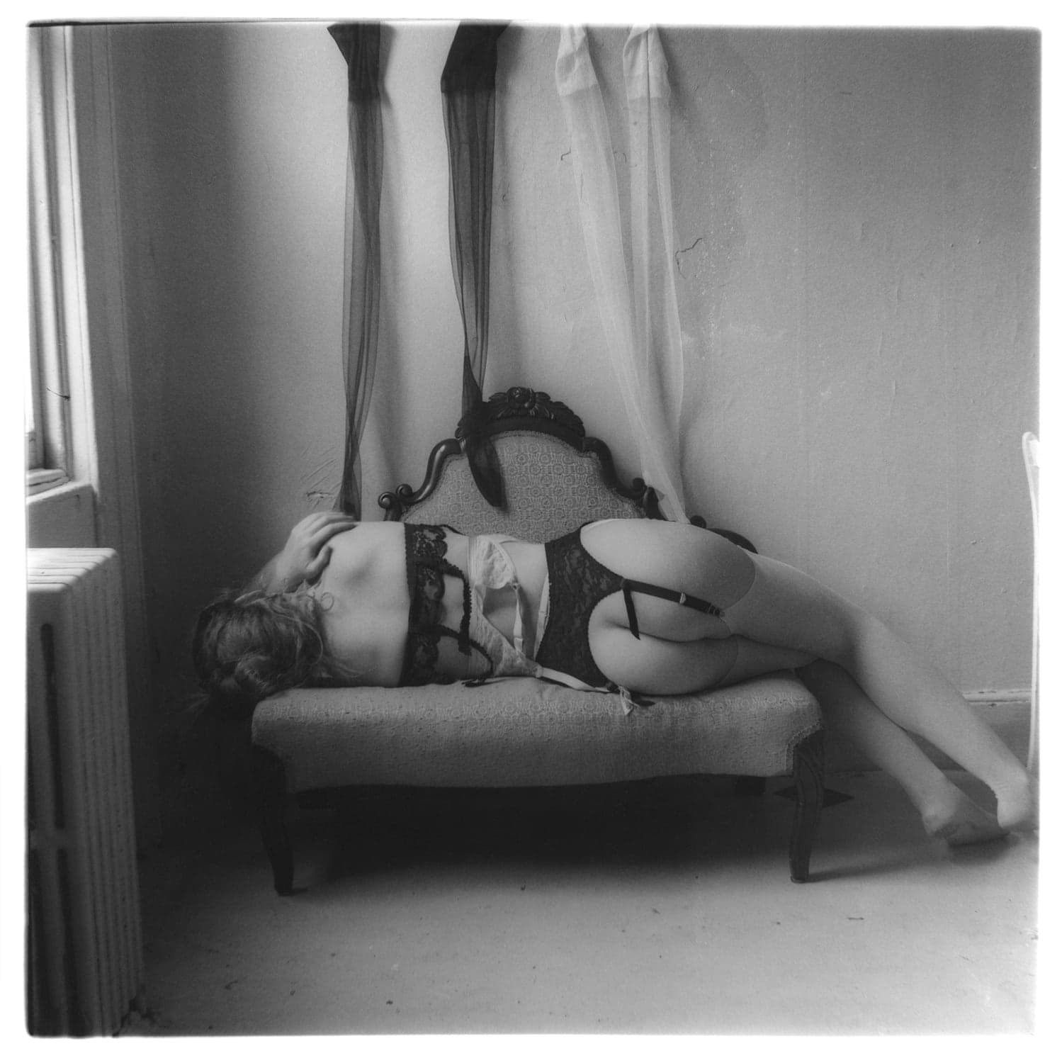 Black and white figure of a figure from behind dressed in lingerie, reclining on a couch by a window.
