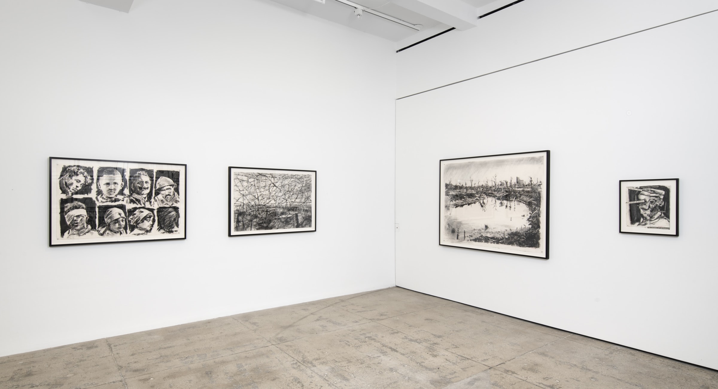 Four graphite drawings of battered children and war-torn landscapes hang in the corner of a room. 