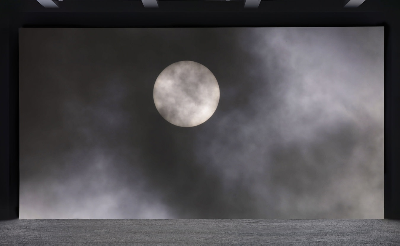 A large projection depicts a bright full moon behind translucent dark clouds. 