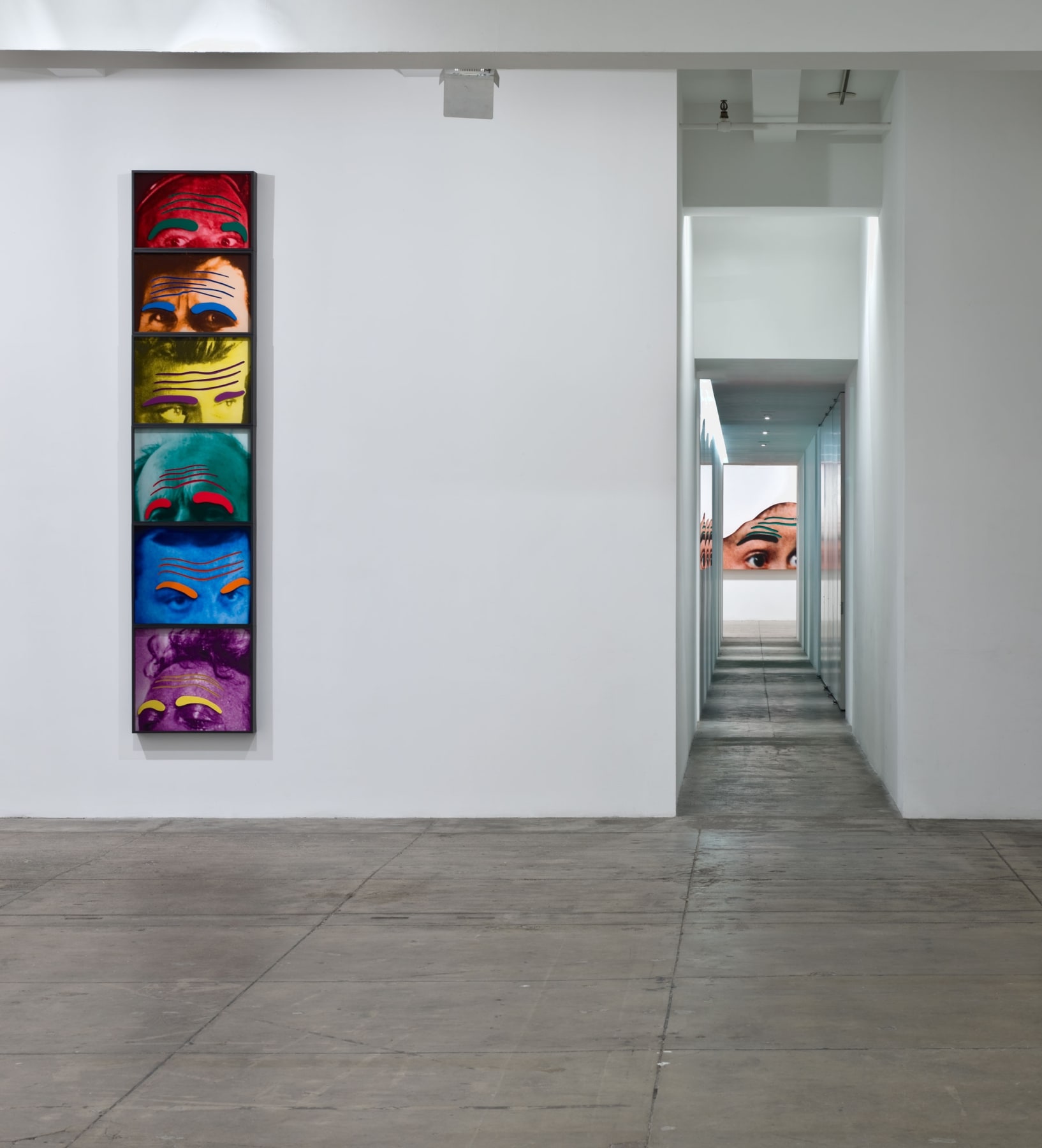 To the left of a long hallway, six framed images of foreheads in different colors are stacked on top of each other. 