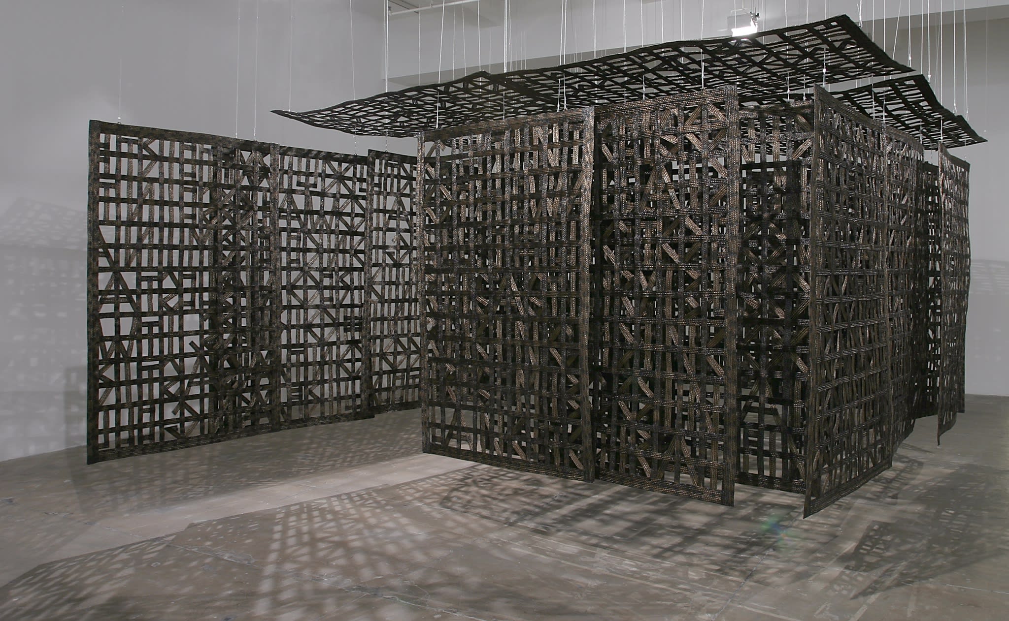 A large wooden sculpture, made up of several panels made up of wooden carved patterns which hang from the ceiling, forming a partially enclosed space.