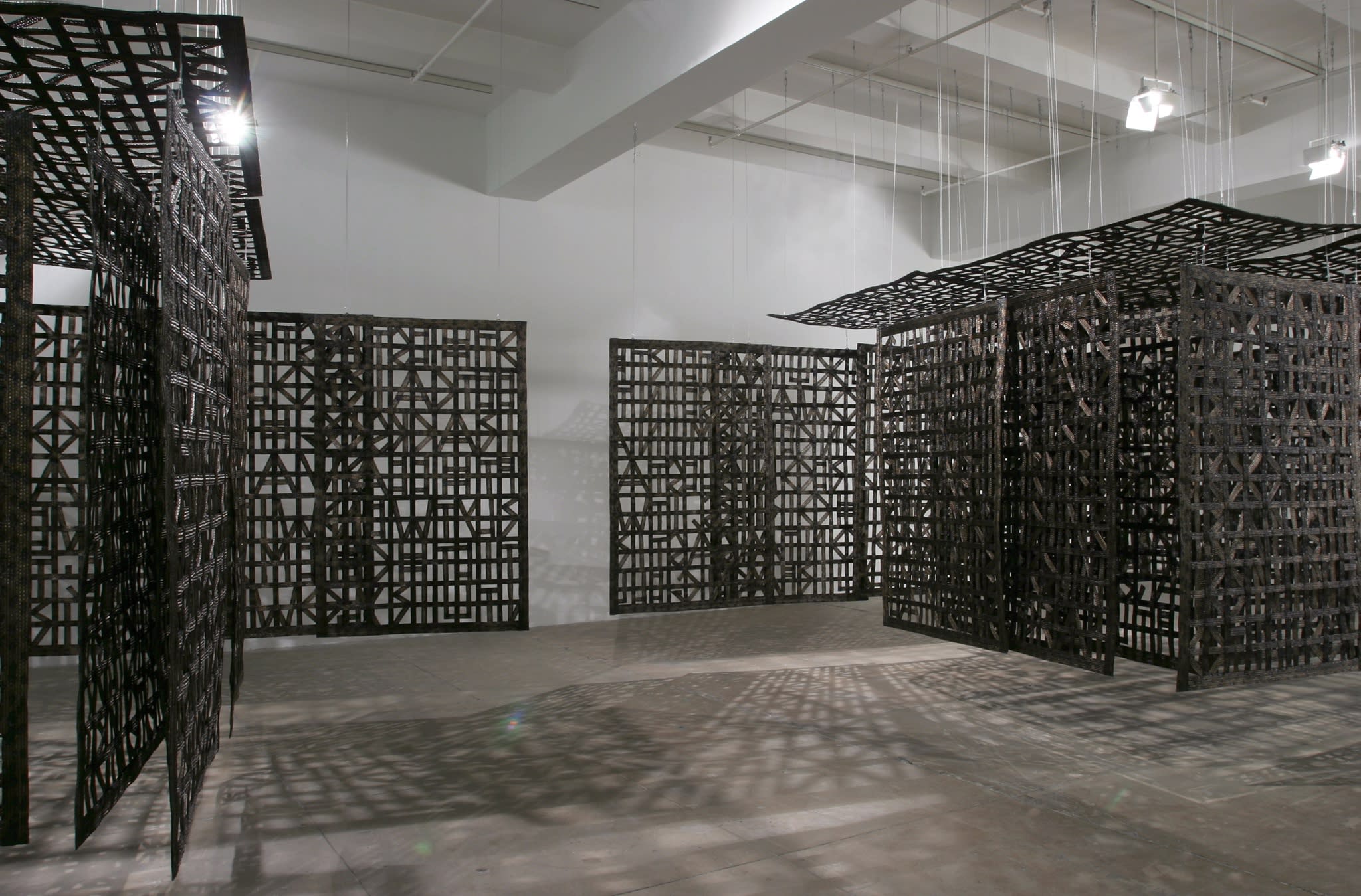 A large wooden sculpture, made up of several panels made up of wooden carved patterns which hang from the ceiling, forming a partially enclosed space.