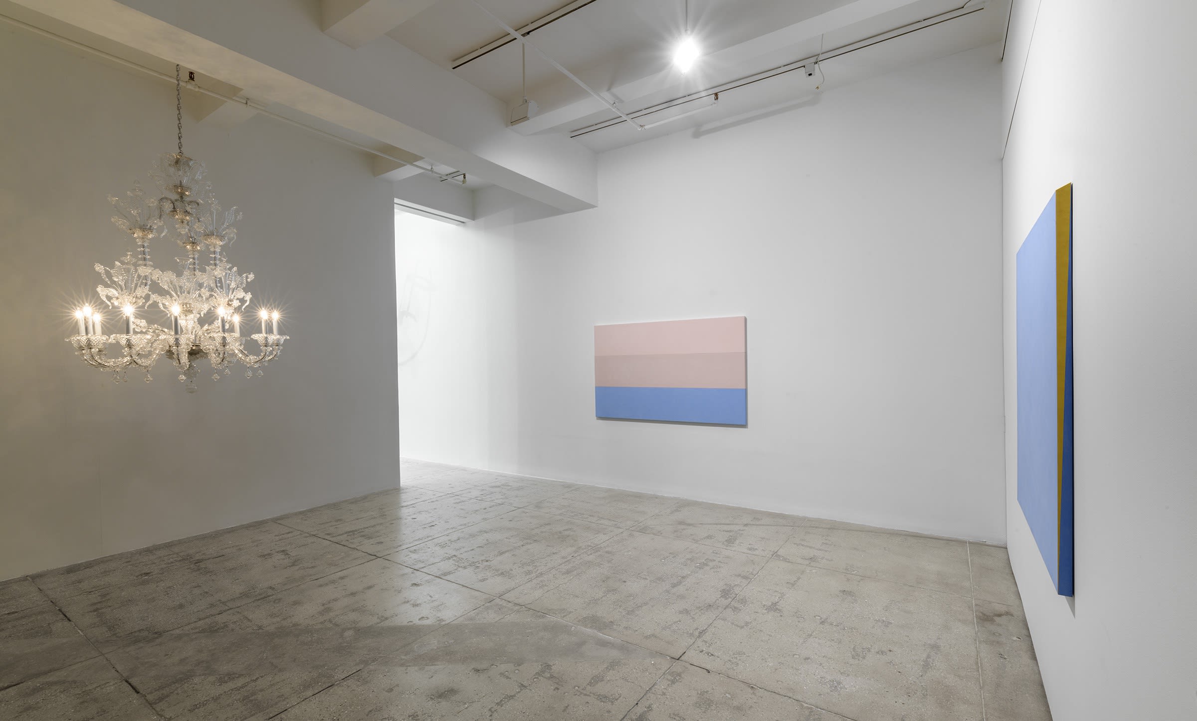 2 blue and pink paintings hang in the gallery; there is a chandelier hanging from the ceiling to the left.