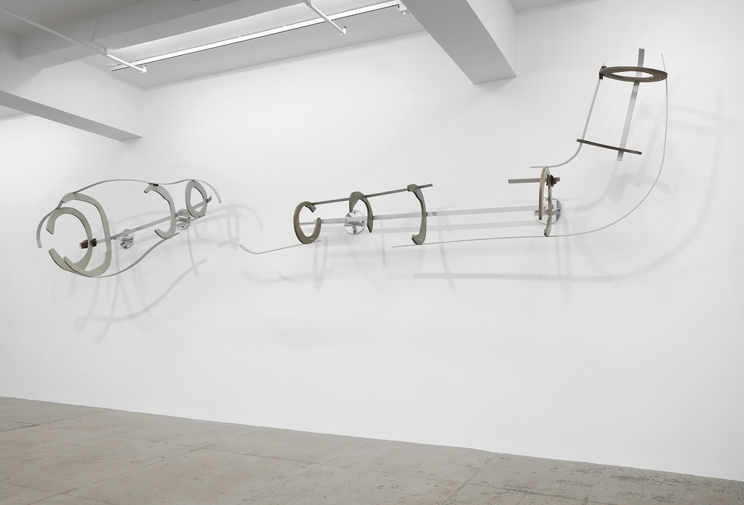 An abstract sculpture is attached to the wall in various pieces connected by thin metal wire.