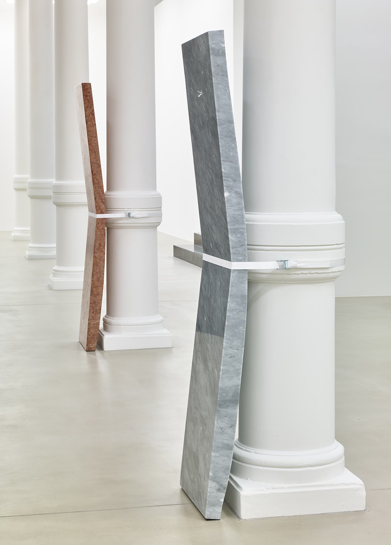 Installation view, slabs of stone strapped to pillars in a row.