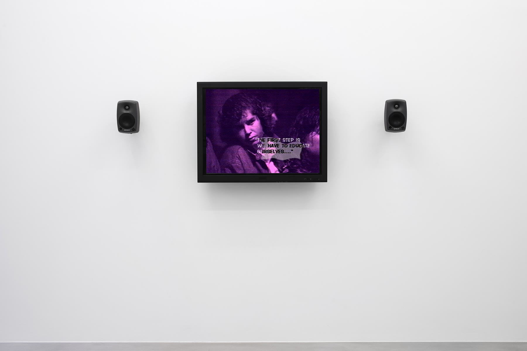 A purple monitor with 2 speakers displays a woman with text reading "The first step is we have to educate ourselves." 
