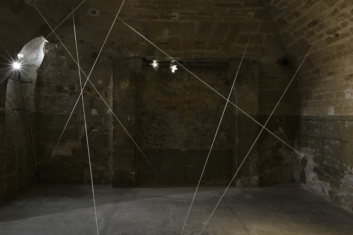White cords are suspended in a dimly lit room with brick walls.