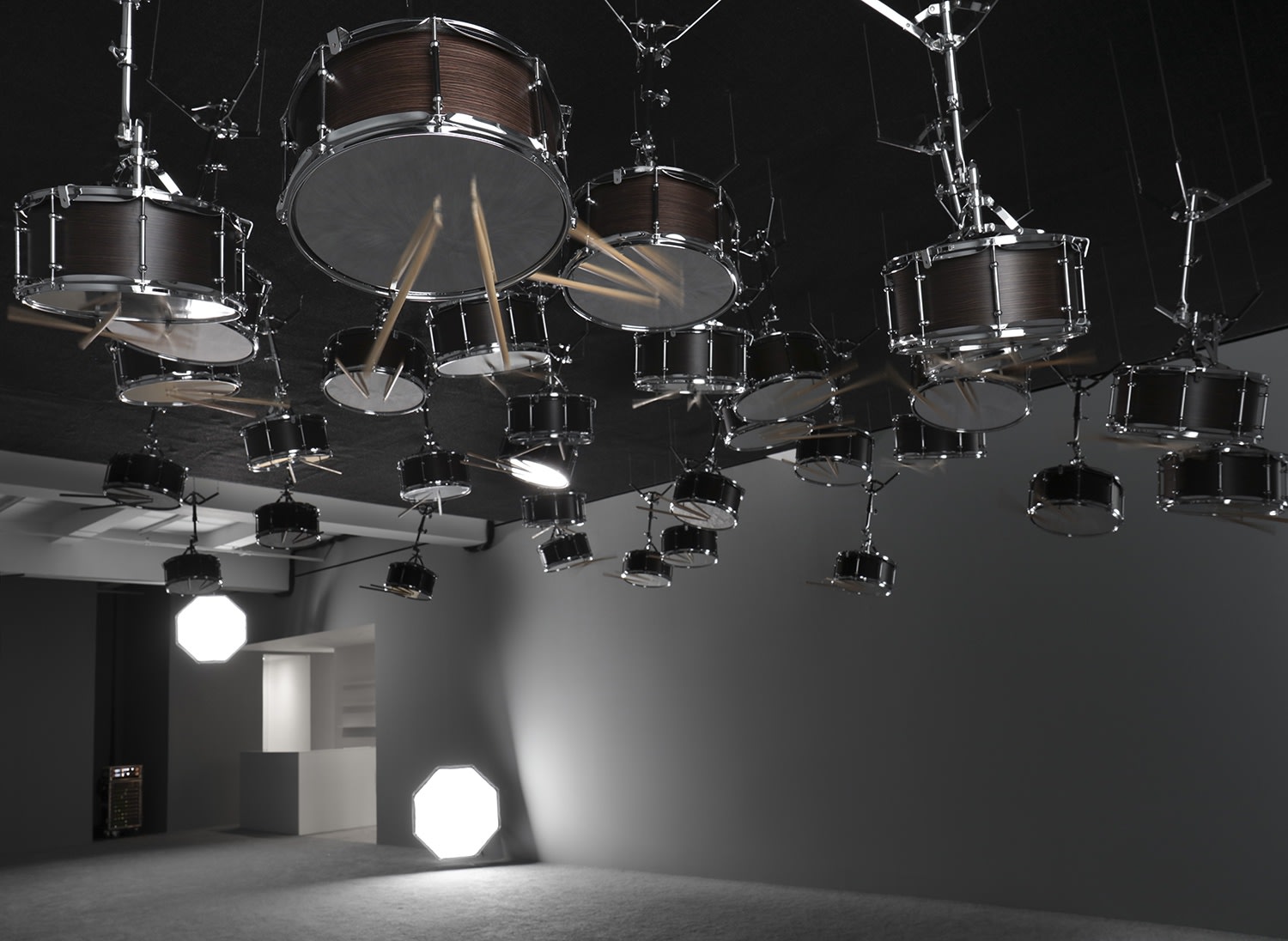 Snare drums suspended upside down from the ceiling in a grey room. 