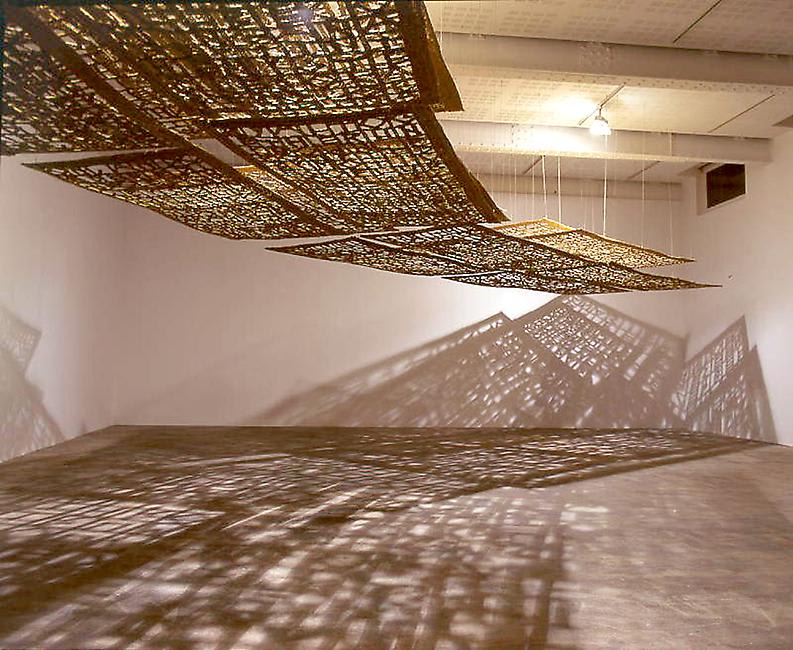 An artwork hanging from the ceiling casts light and shadows across the gallery space. 