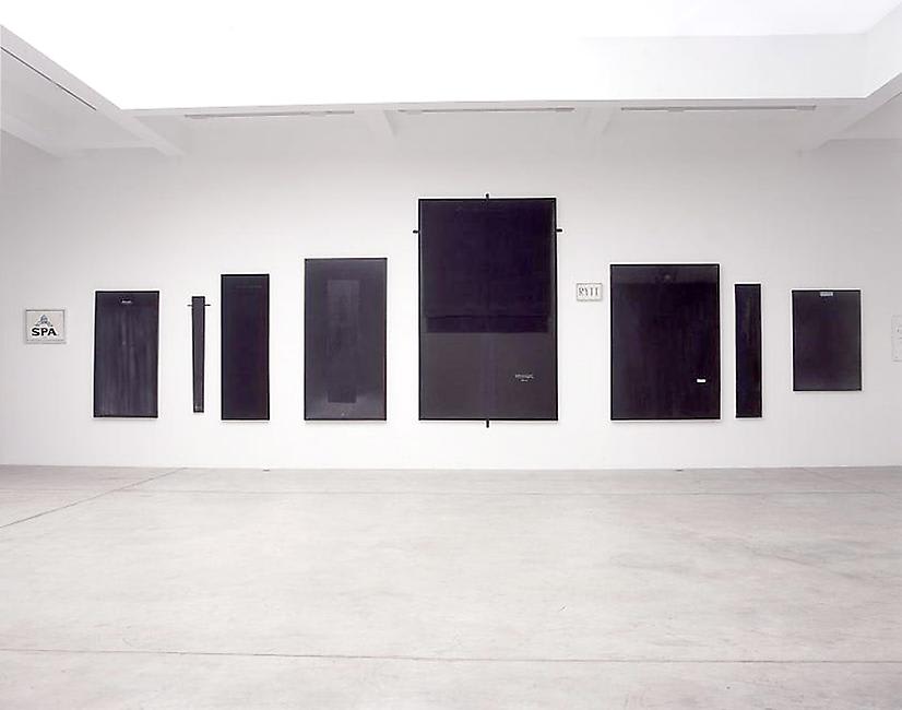 Dark blue framed artworks of various heights hung horizontally on a gallery wall.