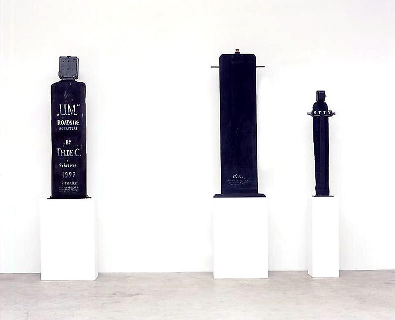 3 large sculptures of bottles sitting on 3 white pedestals. 