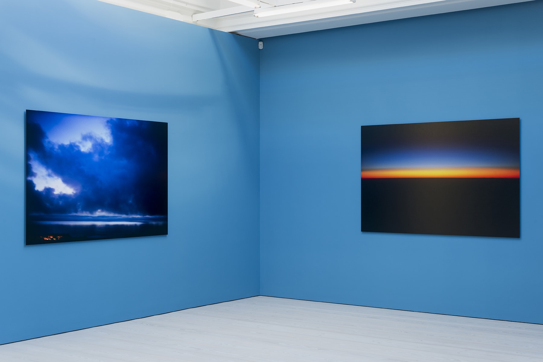 2 large color photographs of horizon lines at sunset hanging on a bright blue wall. 