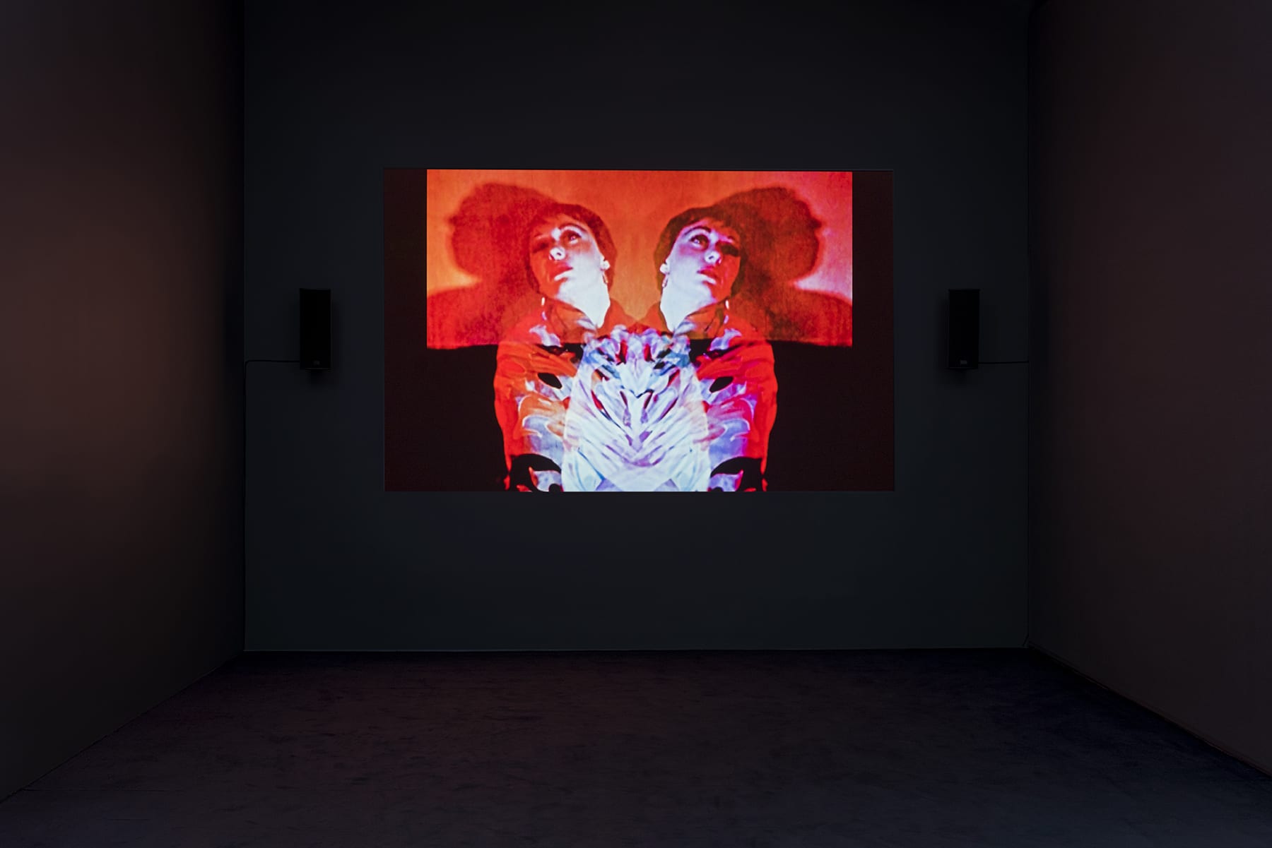 A red projection in a darkened room of a double image of a woman. 