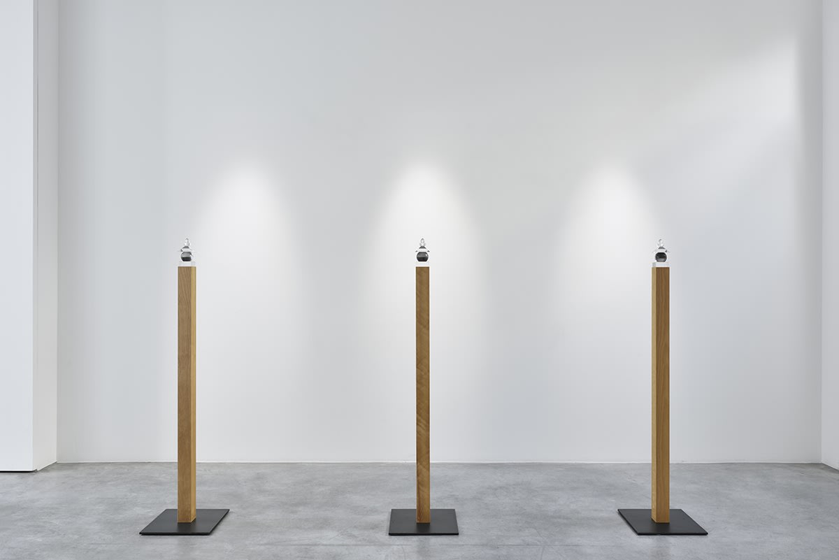 Gallery installation: three wooden planks vertically placed with a small glass orb sculptures resting on top.