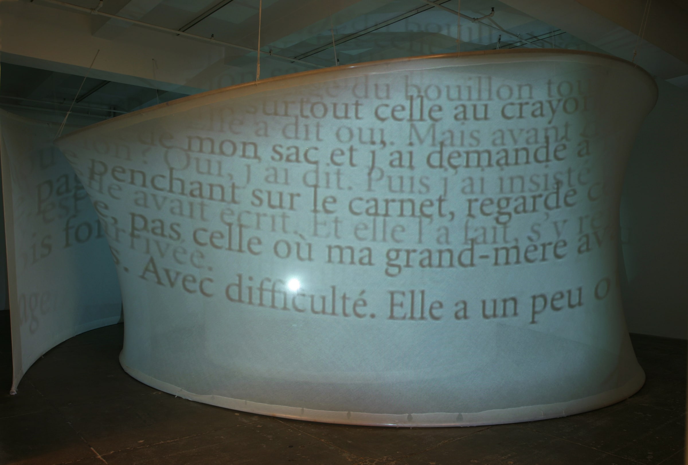 Text in french projected onto a curved, white, translucent piece of fabric stretched from floor to ceiling. 