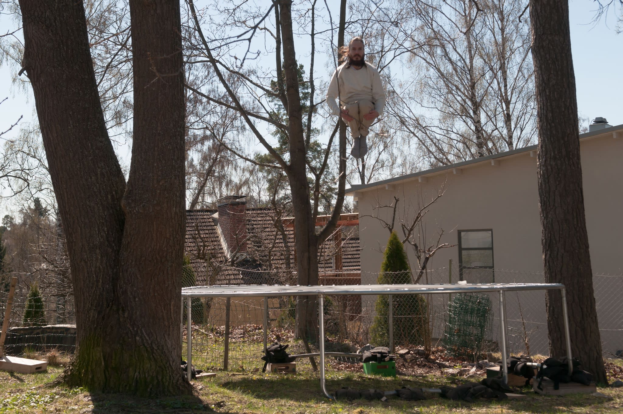 Image of person curled in a ball mid-air from jumping on trampoline in suburban backyard.