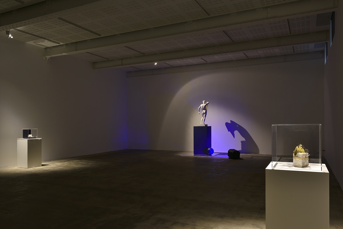 Gallery installation, blue light hits a small Greek statue creating a a hunched shadow against the wall.