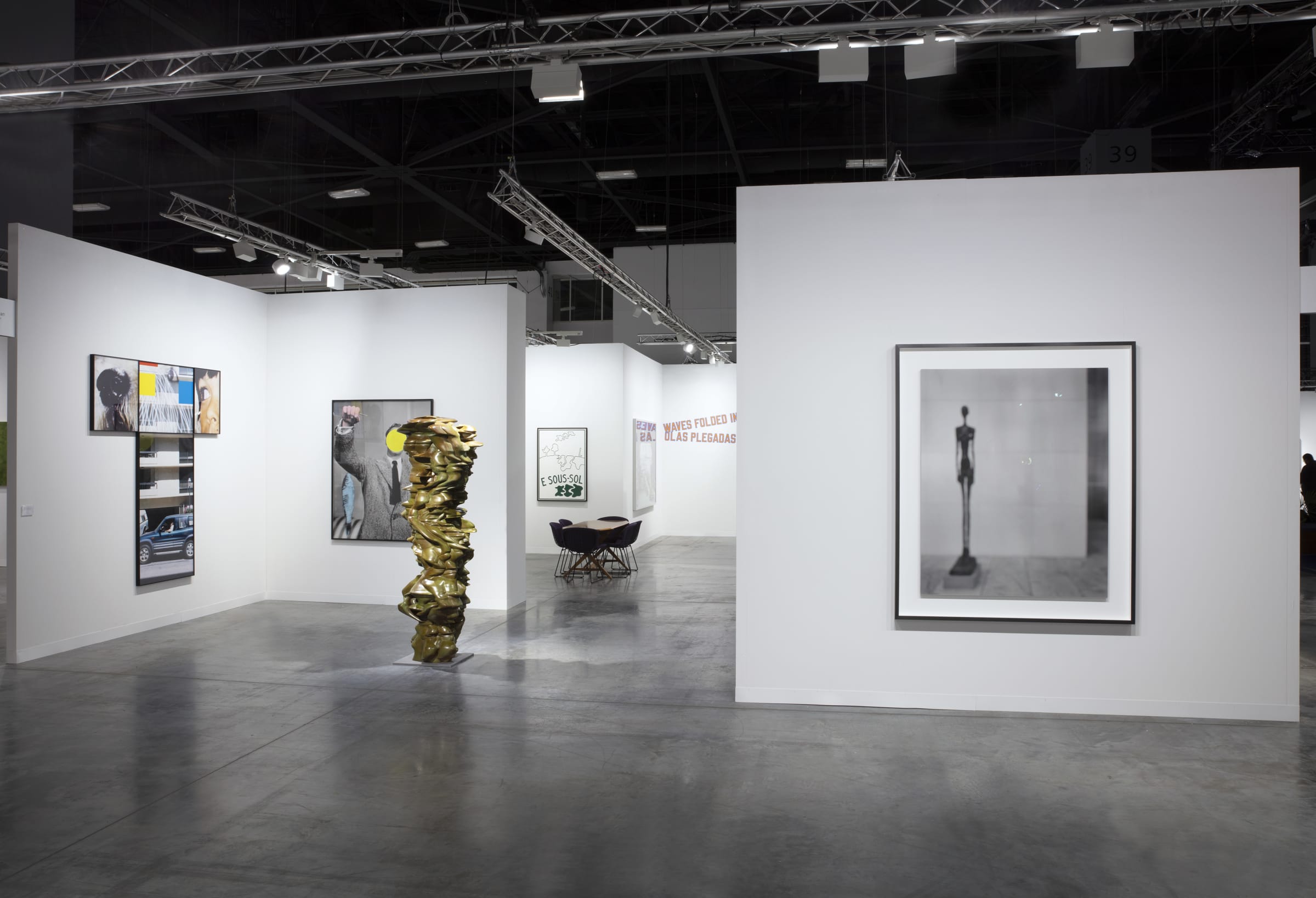 Various artworks hang on white walls in a large warehouse. 