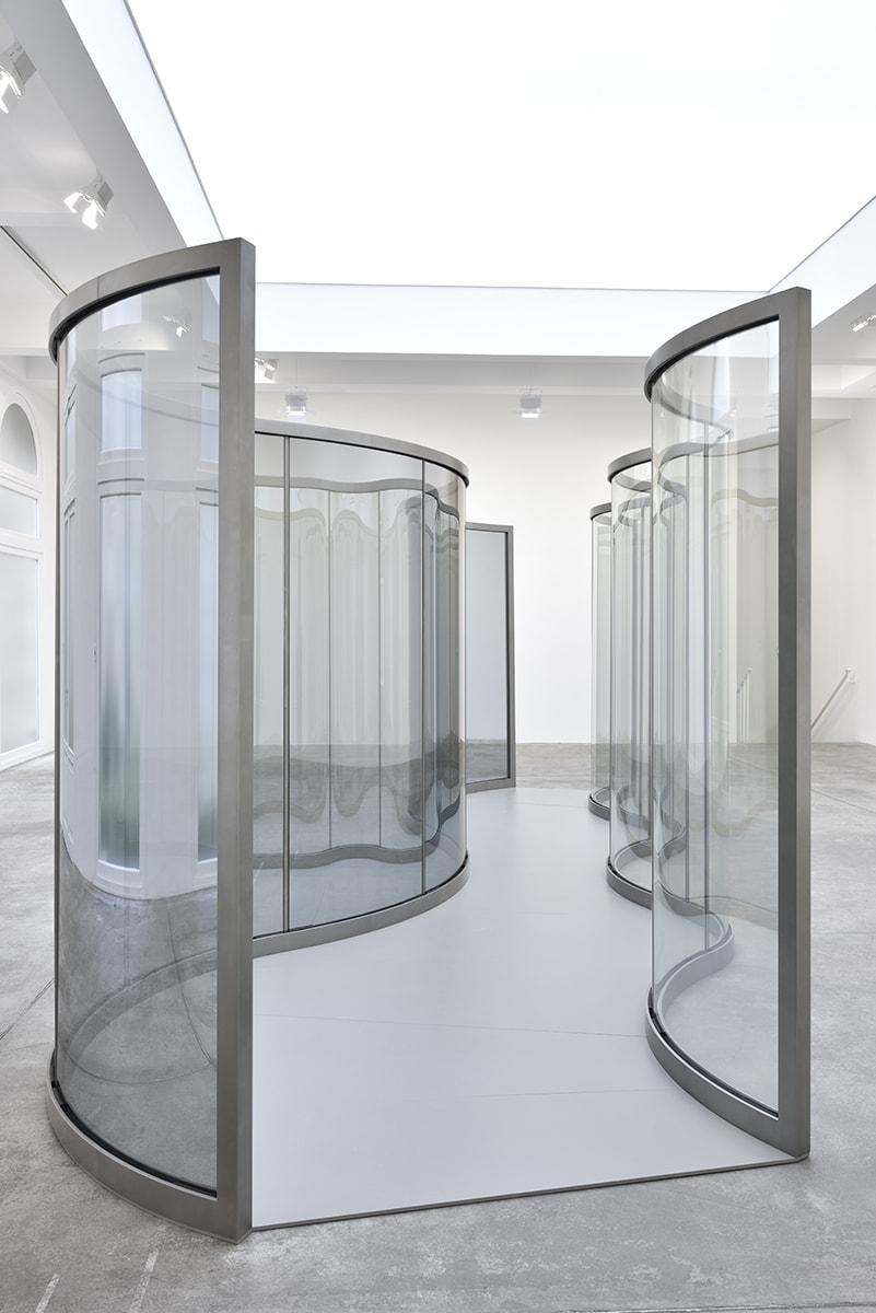 2 wavy panes of glass create a corridor in the center of a bright room. 