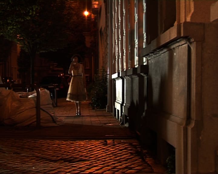 a person walks on a residential sidewalk in a city at night; Chantal Akerman, Femmes d’Anvers en Novembre (Women of Antwerp in November), 2008