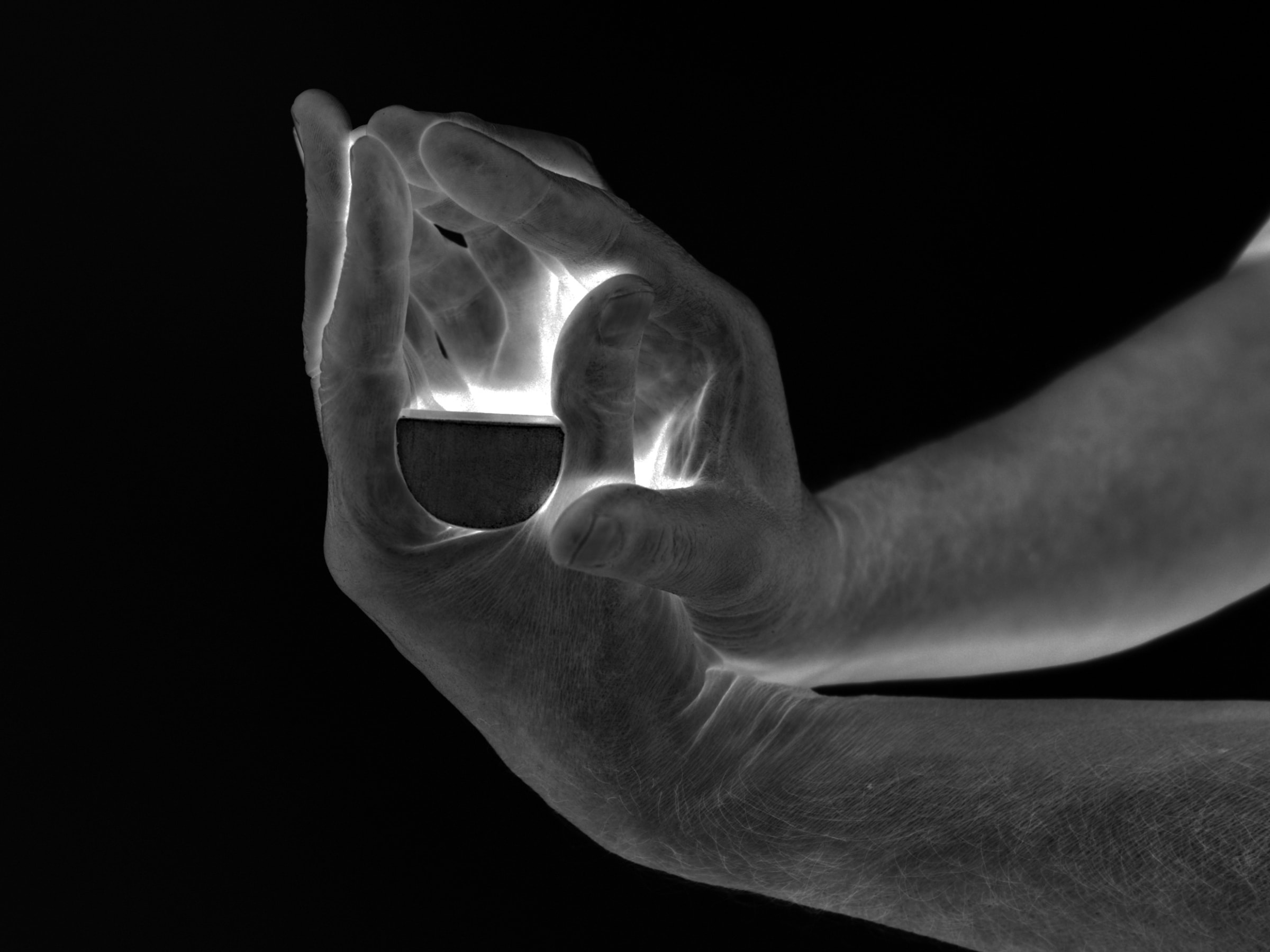 black and white photo of two hands with opposite fingers meeting to form a shape and a light shining through the void
