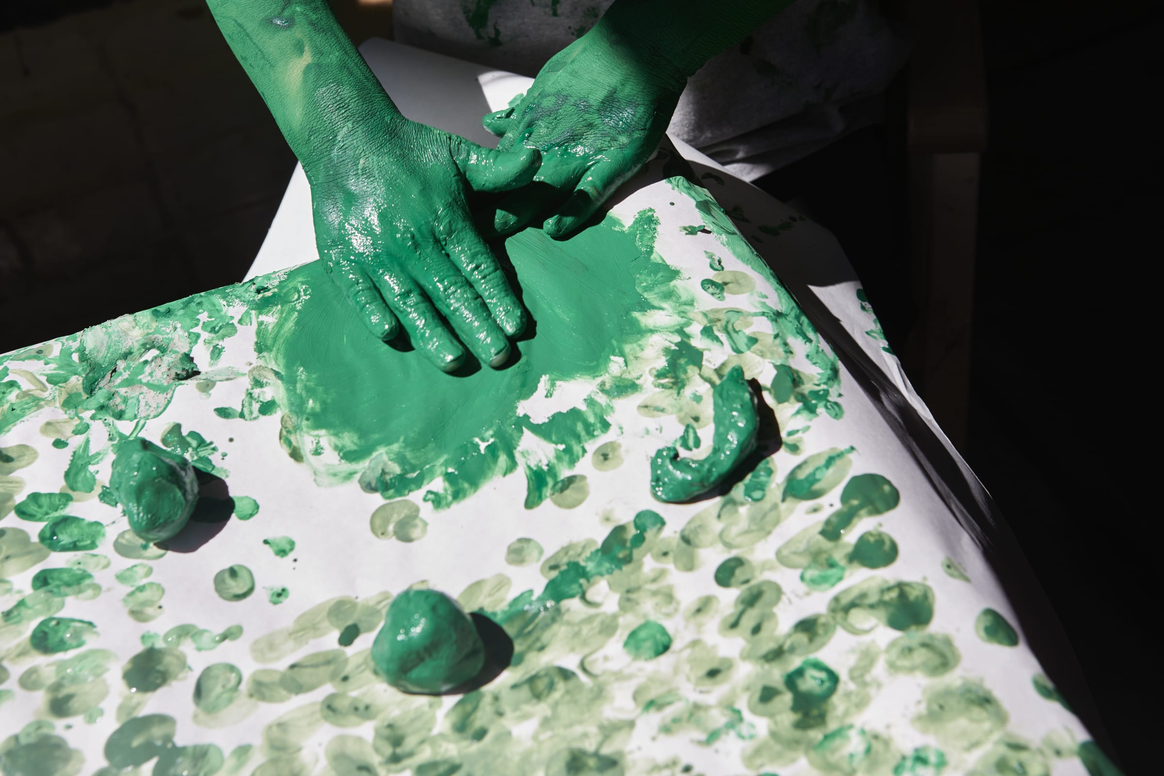A child's hand covered in green paint, finger painting on a large piece of white paper