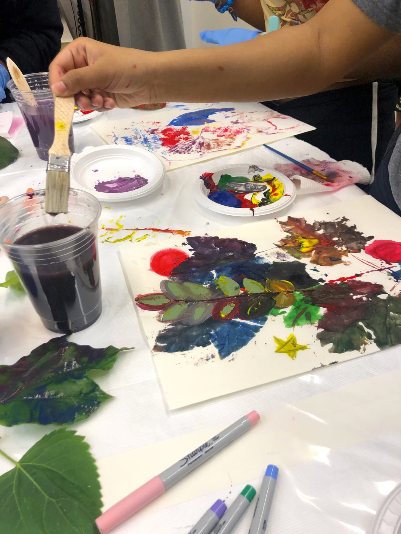 A student holding a paintbrush creates a colorful painting with leaves